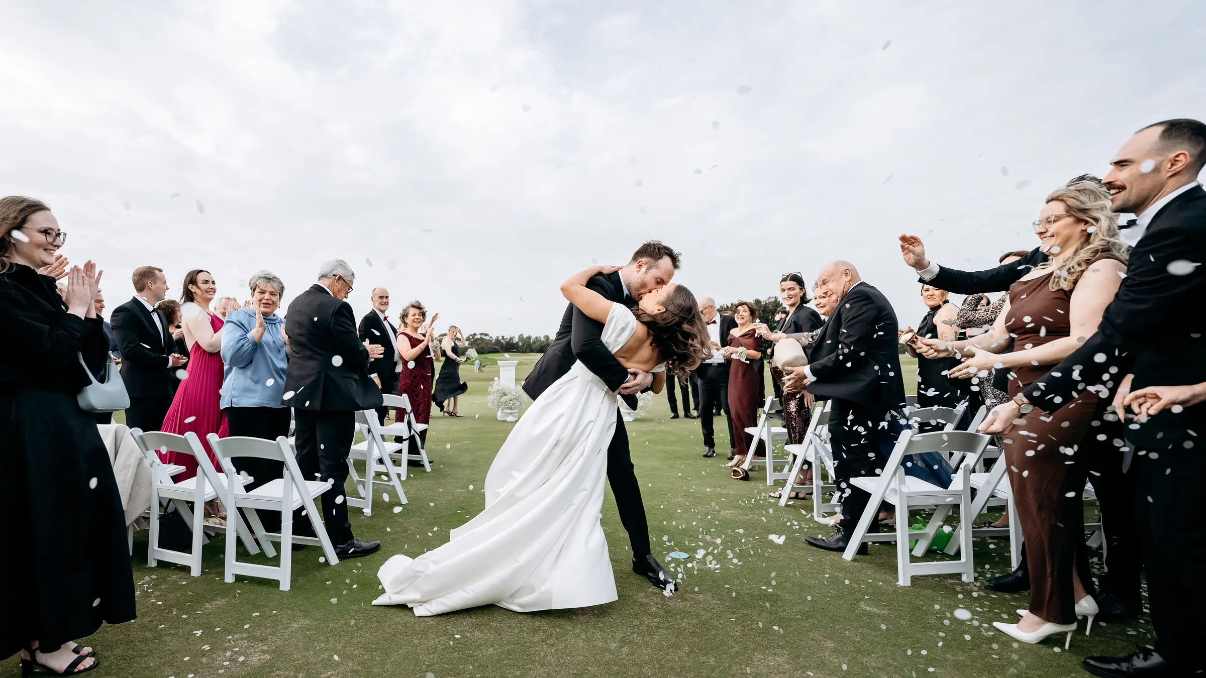 A bride and groom kiss in the aisle as their guests throw confetti